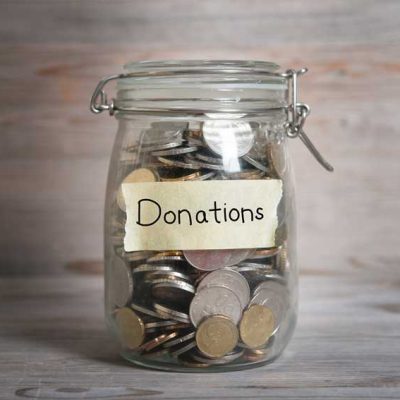 Coins in glass money jar with donations label, financial concept. Vintage wooden background with dramatic light.