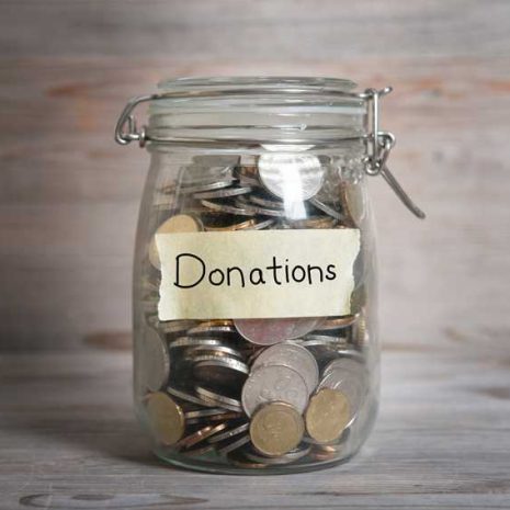 Coins in glass money jar with donations label, financial concept. Vintage wooden background with dramatic light.